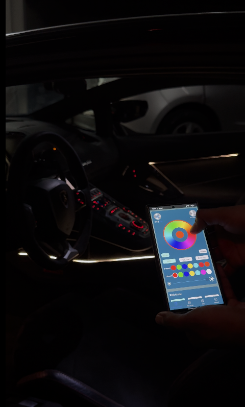 Driver using a smartphone app to control RGB ambient lighting inside a luxury car, with customizable LED interior lights on the dashboard and door panels.